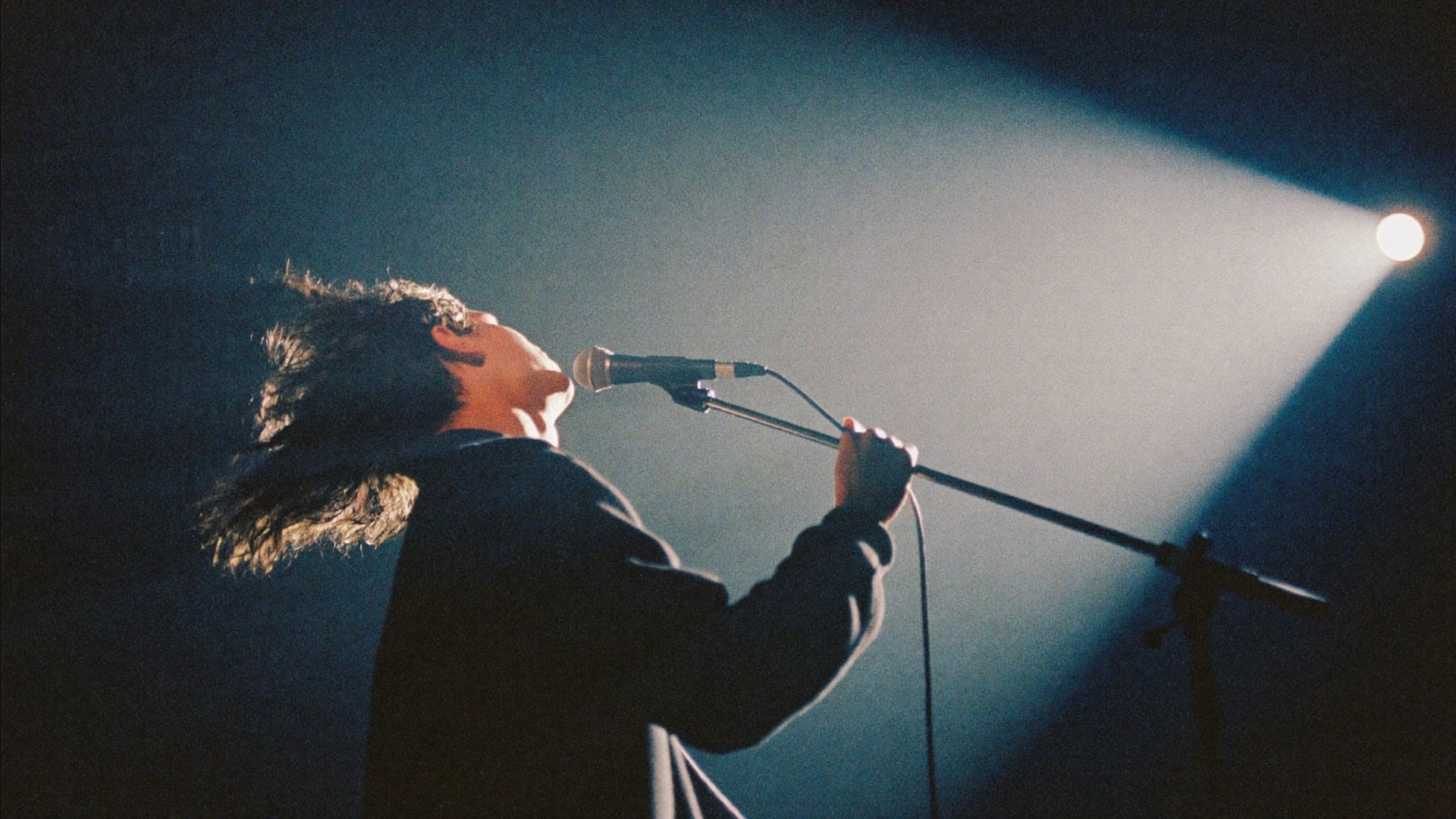 A singer at a vintage microphone under a hard spotlight, mid-note