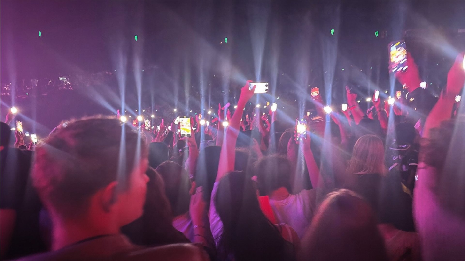 A crowd at a night concert, hands and phone lights raised through haze and coloured beams